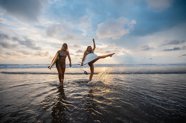 Disparo gran angular de dos mujeres de pie en la playa durante una puesta de sol