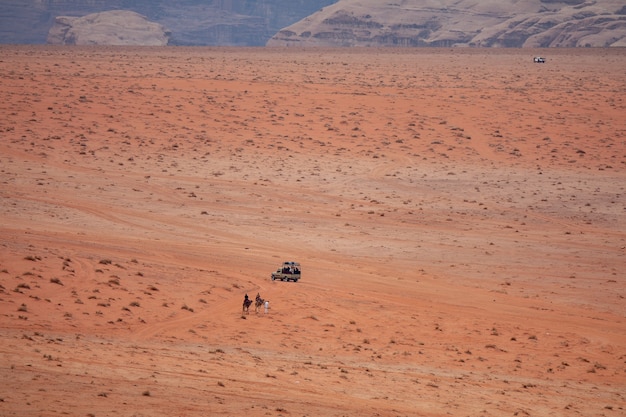 Disparo gran angular de dos personas en camellos acercándose a un coche en un desierto