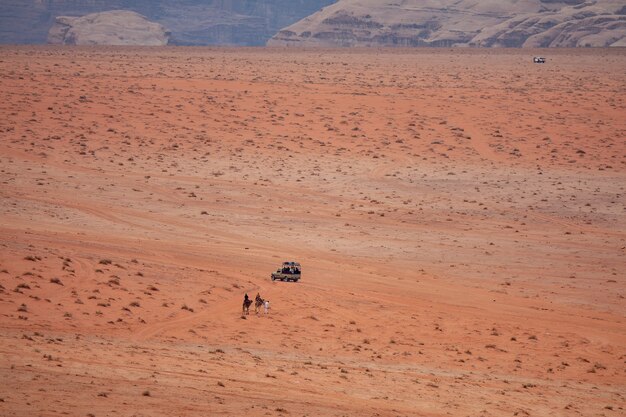 Disparo gran angular de dos personas en camellos acercándose a un coche en un desierto