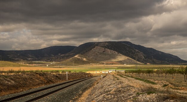 Disparo de gran angular de las vías del tren que van hacia una montaña bajo un cielo nublado