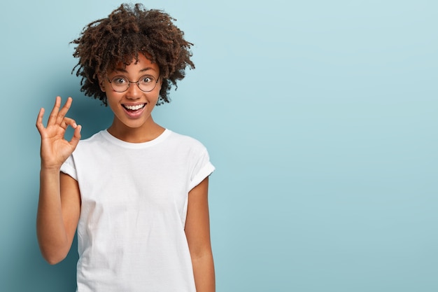 Disparo horizontal de alegre mujer afroamericana hace gesto bien, está de acuerdo con una buena propuesta