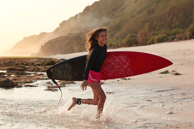 Disparo horizontal de alegre surfista experimentado corre sobre el agua, expresa emociones positivas