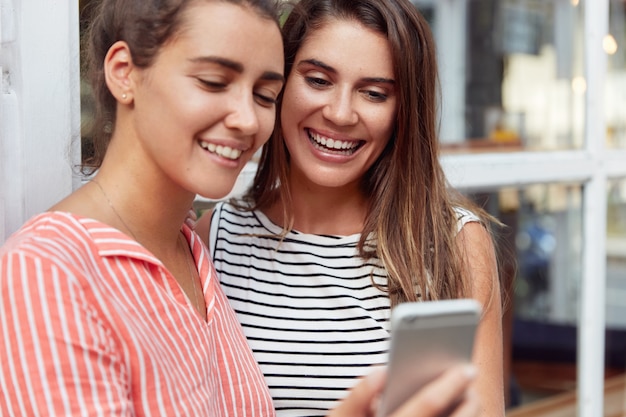 Disparo horizontal de amigas jóvenes felices ver la pantalla del teléfono inteligente