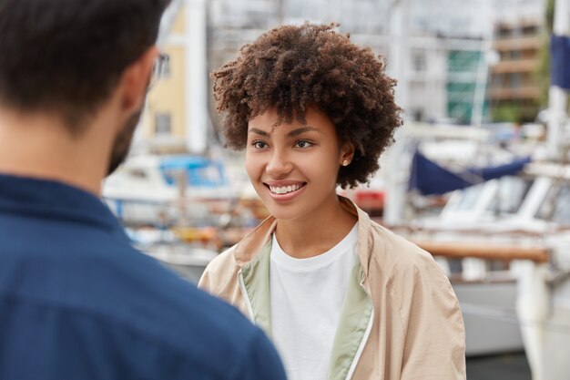 Disparo horizontal de atractiva chica afroamericana tiene una apariencia agradable, sonrisa con dientes