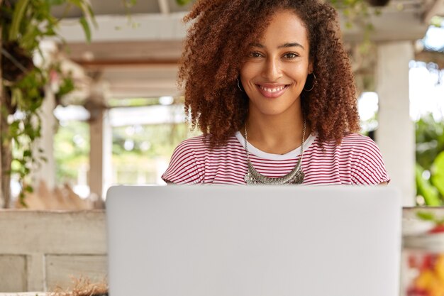 Disparo horizontal de bonita mujer independiente se sienta delante de la computadora portátil abierta