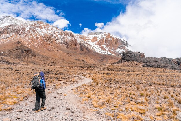 Disparo horizontal de un excursionista con mochila de senderismo en un campo seco rodeado de rocas y montañas