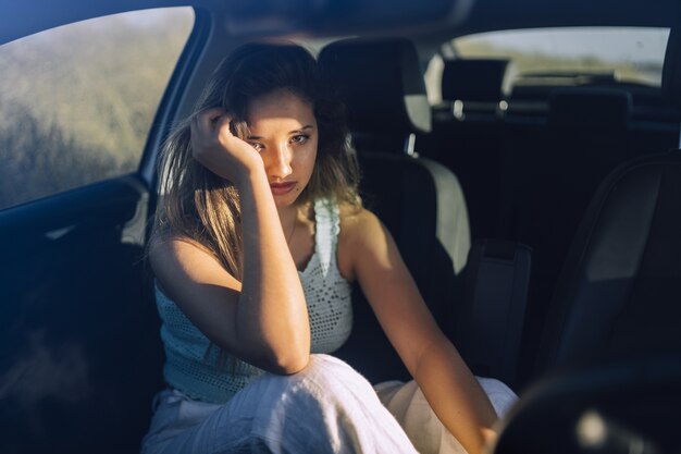 Disparo horizontal de una hermosa joven mujer caucásica posando en el asiento delantero de un coche en un campo