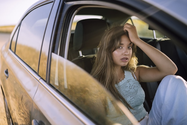 Foto gratuita disparo horizontal de una hermosa joven mujer caucásica posando en el asiento delantero de un coche en un campo