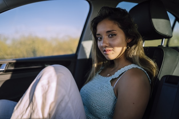 Disparo horizontal de una hermosa joven mujer caucásica posando en el asiento delantero de un coche en un campo