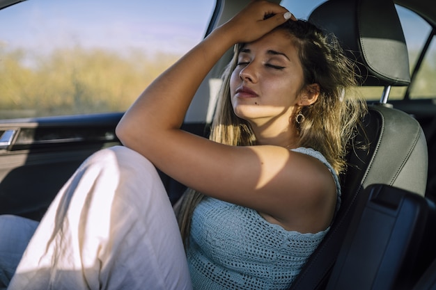 Disparo horizontal de una hermosa joven mujer caucásica posando en el asiento delantero de un coche en un campo