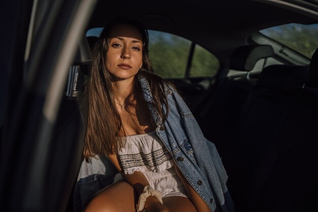 Disparo horizontal de una hermosa joven mujer caucásica posando en el asiento trasero de un coche en un campo