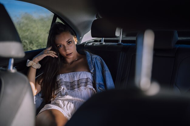 Disparo horizontal de una hermosa joven mujer caucásica posando en el asiento trasero de un coche en un campo
