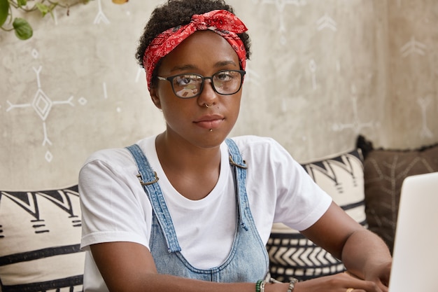 Disparo horizontal de hermosa mujer negra con estilo lleva gafas y diadema roja