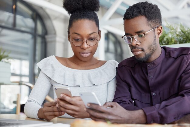 Disparo horizontal de hombres y mujeres jóvenes de piel oscura que escriben notificaciones de texto en teléfonos inteligentes, chatean en línea