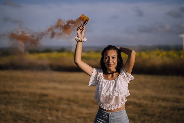 Disparo horizontal de una joven mujer caucásica posando con una bomba de humo en un campo