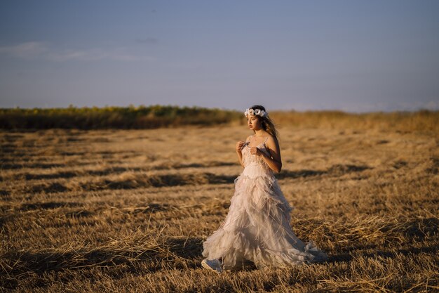 Disparo horizontal de una joven mujer caucásica con un vestido blanco posando en un campo