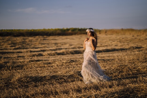 Disparo horizontal de una joven mujer caucásica con un vestido blanco posando en un campo
