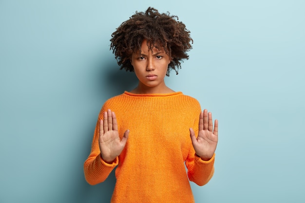 Foto gratuita disparo horizontal de mujer afroamericana seria muestra gesto de parada, estira las palmas hacia la cámara, prohíbe acercarse, dice que es suficiente