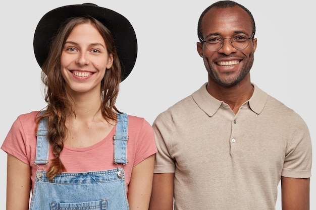 Foto gratuita disparo horizontal de mujer y hombre multiétnicos parados juntos contra la pared blanca, sonreír ampliamente, aislado