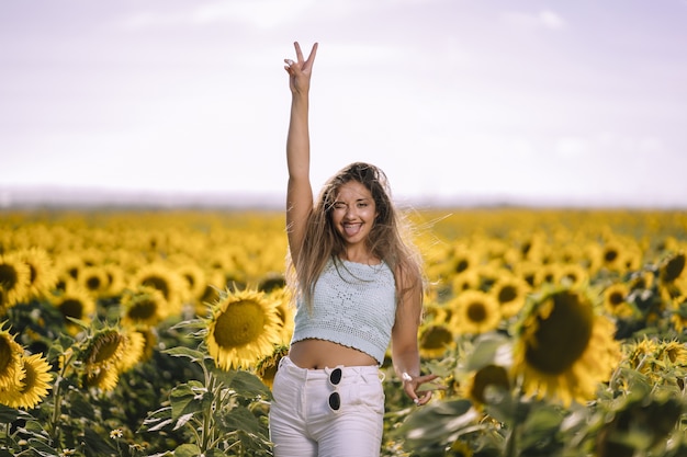 Disparo horizontal de una mujer joven caucásica posando en un brillante campo de girasoles en un día soleado