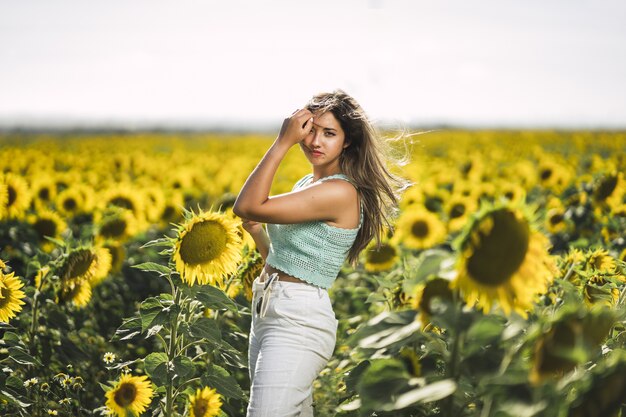 Disparo horizontal de una mujer joven caucásica posando en un brillante campo de girasoles en un día soleado