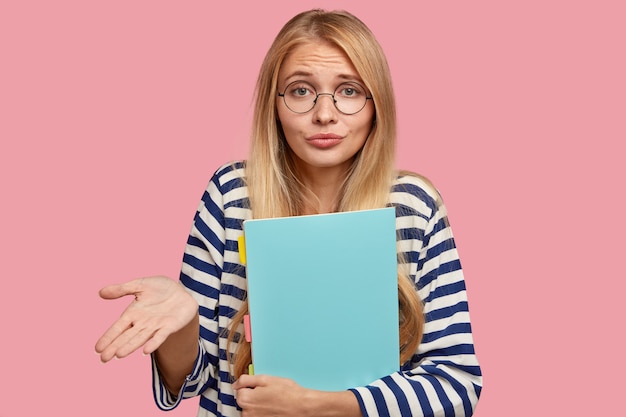 Disparo horizontal de mujer rubia despistada sujeta la palma con vacilación, lleva gafas transparentes redondas