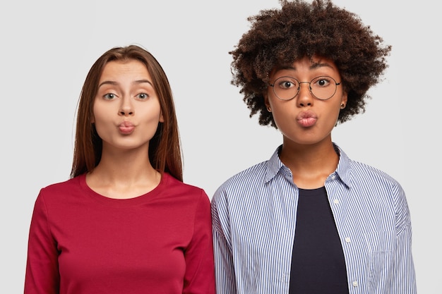 Foto gratuita disparo horizontal de mujeres bonitas que besan con los labios, miran con expresión encantada, vestidas con ropa casual