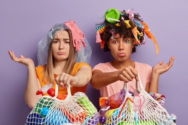 Disparo horizontal de mujeres jóvenes deprimidas posando con basura sobre ellos