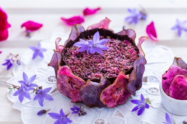 Disparo horizontal de un pastel morado vegano crudo de pera con peras deshidratadas sobre una mesa blanca - vegano