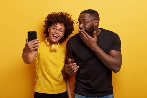 Disparo horizontal de pose femenina y masculina de piel oscura alegre para hacer retrato selfie