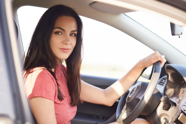 Disparo de lado de buena chica morena seria conduce coche profesionalmente