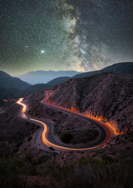 Disparo de larga exposición vertical de un camino en las montañas bajo un cielo estrellado