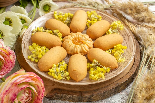 Foto gratuita disparo lateral de un plato de galletas en un plato de madera y flores a su alrededor en mármol