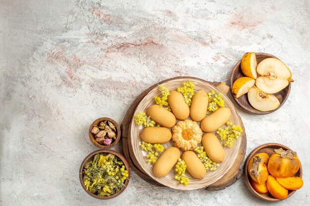 Disparo lejano de un plato de galletas en un plato de madera y tazones de frutas y flores secas a su alrededor