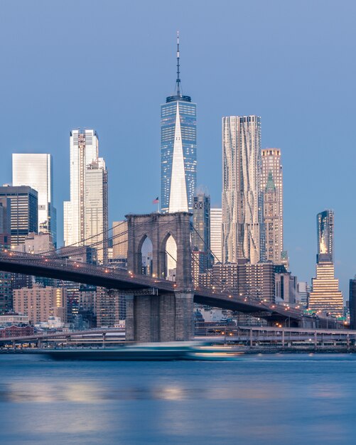 Disparo lejano vertical del puente de Brooklyn en el cuerpo de agua cerca de rascacielos en Nueva York