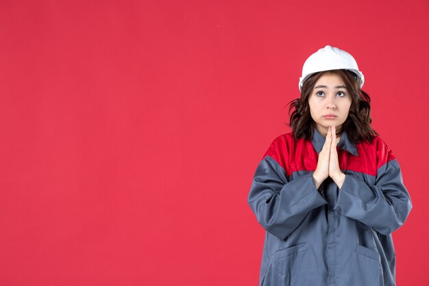 Disparo de medio cuerpo de pensamiento constructor femenino en uniforme con casco y soñando sobre fondo rojo aislado