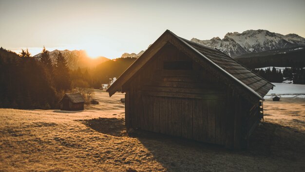 Disparo de una pequeña casa de madera con hierba seca a su alrededor durante el atardecer con montañas en el centrico