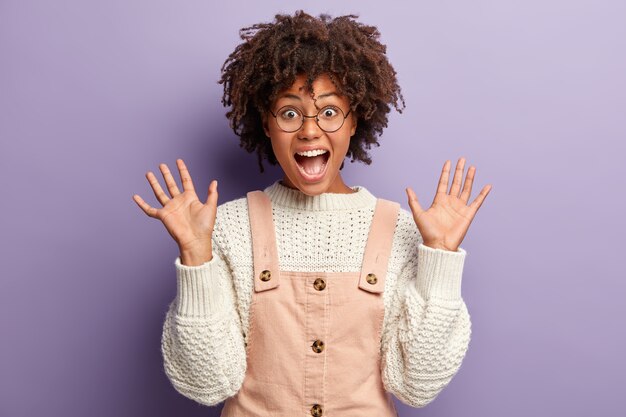 Disparo sincero de una mujer joven de piel oscura alegre y exagerada con cabello afro, levanta dos palmas