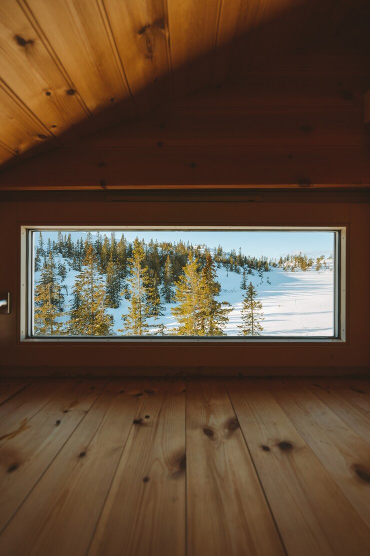 Foto gratuito disparo vertical de un acogedor ático con una ventana con la vista de un bosque cubierto de nieve en noruega