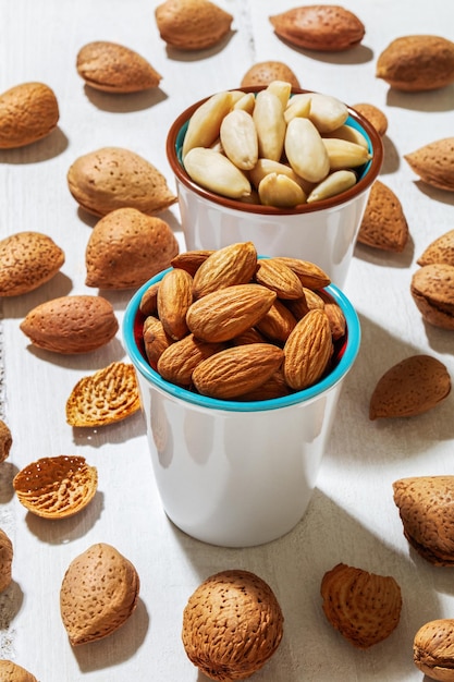 Foto gratuita disparo vertical de almendras en tazas y esparcidas sobre una superficie blanca