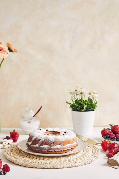 Disparo vertical de un anillo de pastel con frutas y polvo sobre una mesa blanca con blanco