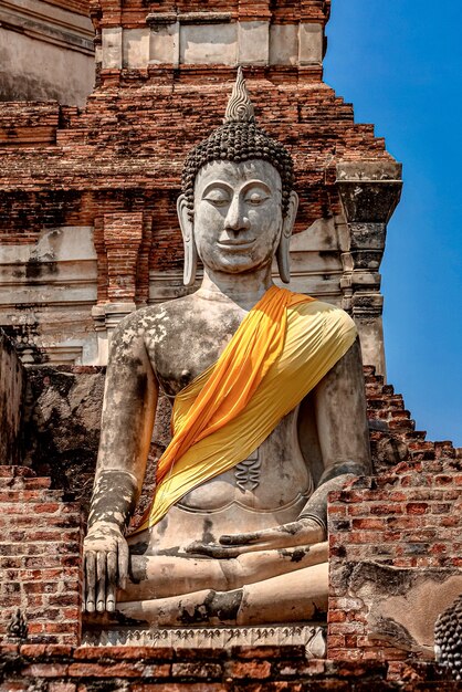 Disparo vertical de una antigua estatua de Buda cubierta con un paño amarillo y naranja