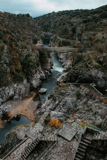 Disparo vertical de un antiguo puente de piedra sobre el río rodeado de rocas cubiertas de musgo