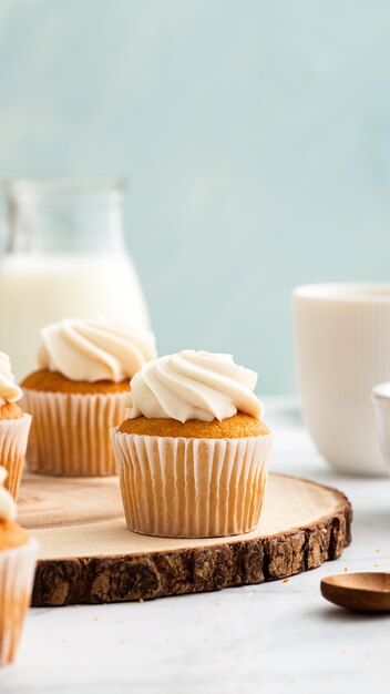 Disparo vertical de apetitosos cupcakes con crema en la parte superior sobre una rodaja de tronco de madera