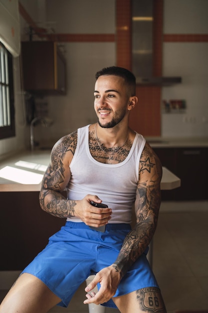 Disparo vertical de un atleta masculino caucásico tatuado sentado en la cocina