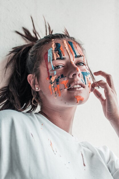 Foto gratuita disparo vertical de una atractiva mujer con pinturas de diferentes colores en su rostro