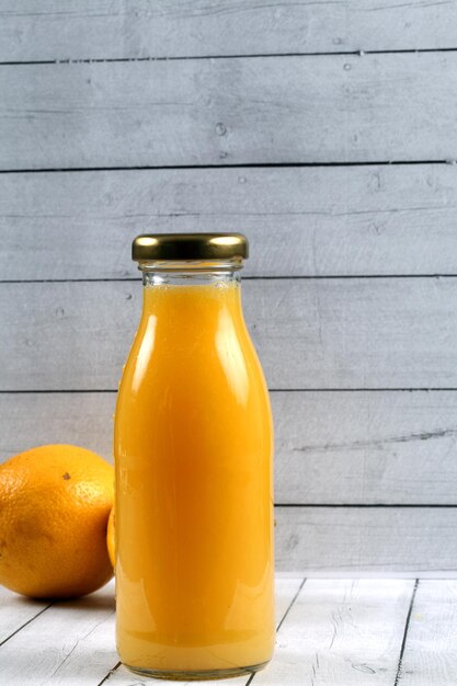 Disparo vertical de una botella de jugo de naranja fresco y naranjas sobre una superficie de madera