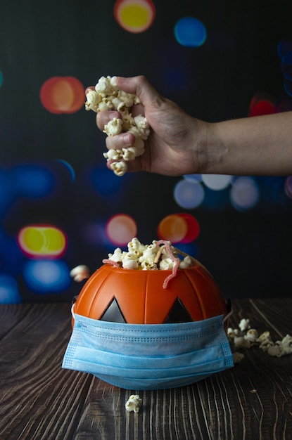 Foto gratuita disparo vertical de una calabaza de halloween con palomitas de maíz y una mascarilla sanitaria