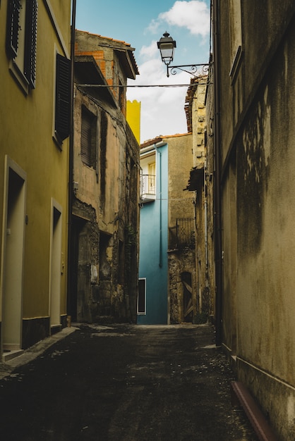 Disparo vertical de un callejón vacío alineado con viejos edificios amarillos que conducen a un edificio azul