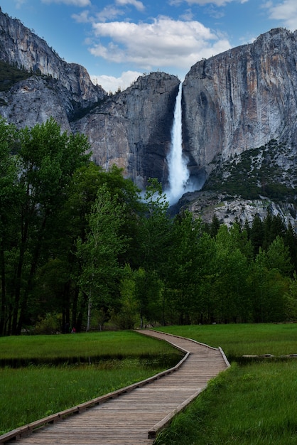 Foto gratuita disparo vertical de un camino que conduce a una cascada bajo un cielo nublado azul